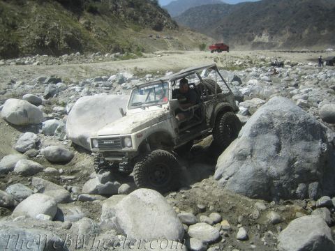 1987 Suzuki Samurai - A modified 1987 Suzuki Samurai tackles a challenging rocky riverbed with a driver inside.