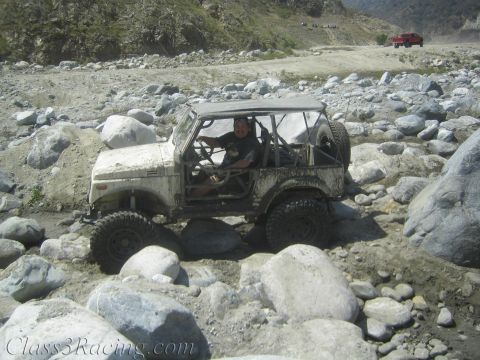 1987 Suzuki Samurai - Suzuki Samurai tackling rough terrain in a rocky riverbed, with another vehicle in the distance.