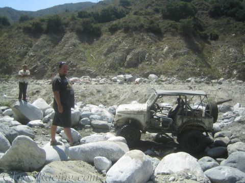 1987 Suzuki Samurai - A modified off-road vehicle sits in a rocky terrain, with two men standing nearby.