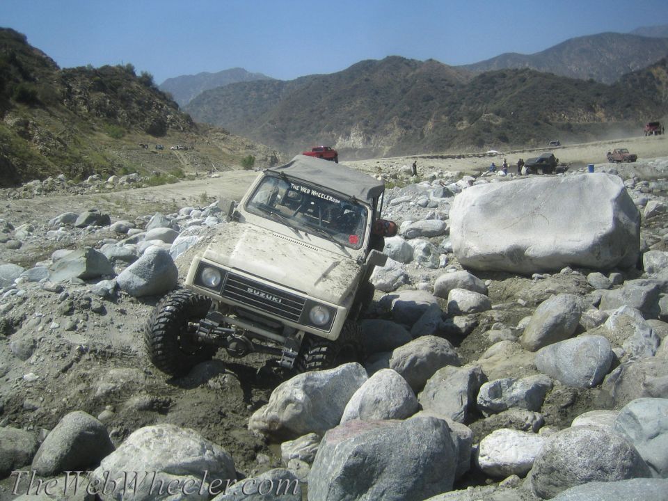 1987 Suzuki Samurai navigating a rocky, off-road trail. The vehicle is tilted as it goes over large stones