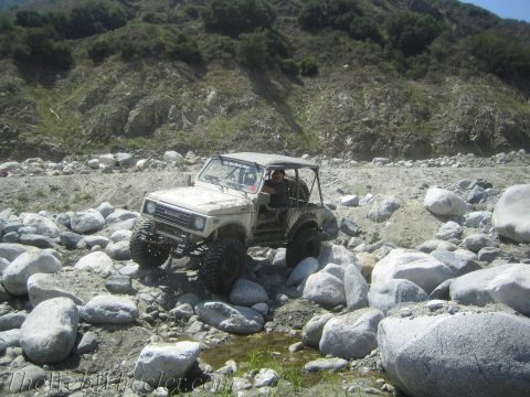 1987 Suzuki Samurai - A 1987 Suzuki Samurai is shown off-roading through a rocky terrain with a driver behind the wheel.