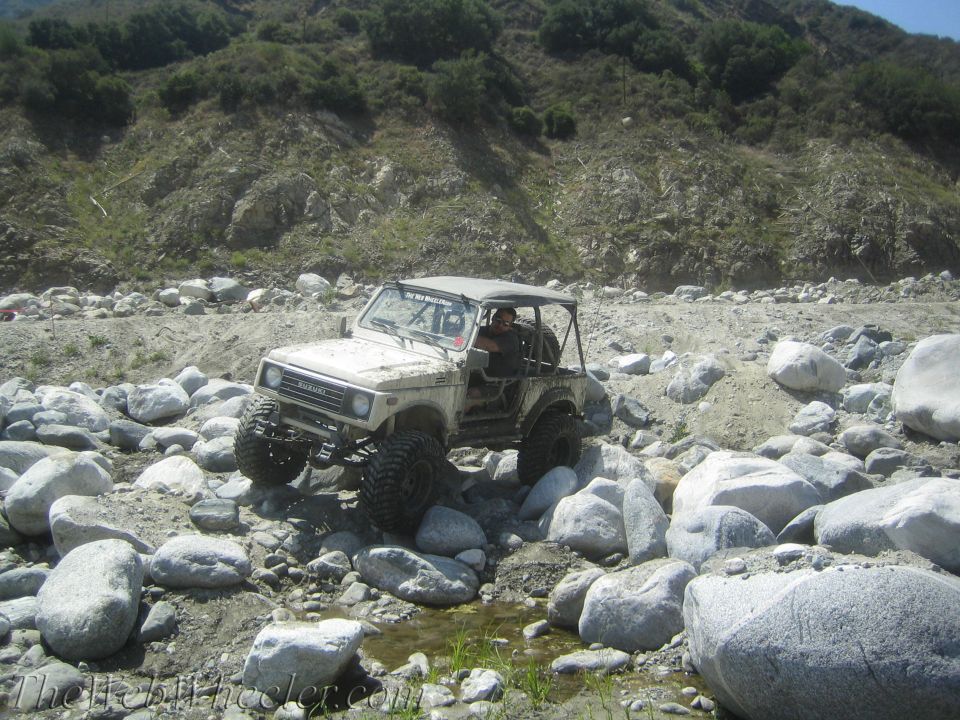 Suzuki Samurai navigating a rocky riverbed with a driver visible