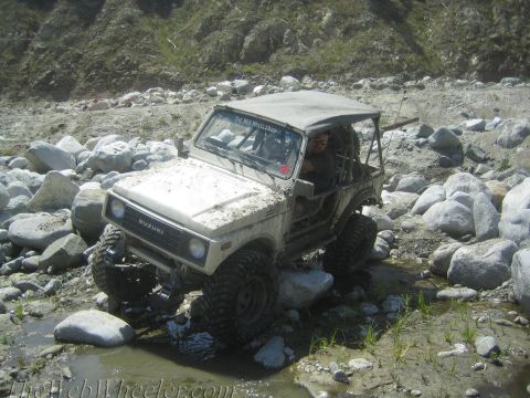 1987 Suzuki Samurai - A white 1987 Suzuki Samurai is shown off-roading through a rocky stream bed.