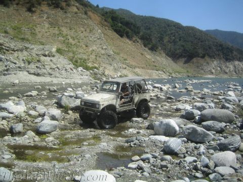 1987 Suzuki Samurai - Suzuki Samurai navigating a challenging rocky terrain near a body of water.