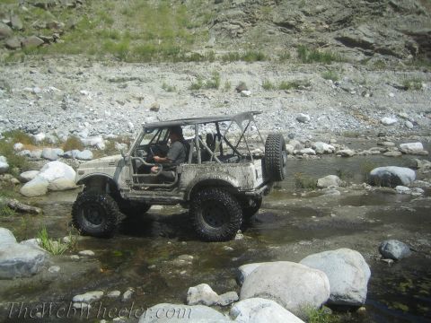 1987 Suzuki Samurai - A white Suzuki Samurai navigates a shallow, rocky riverbed with a driver visible inside.