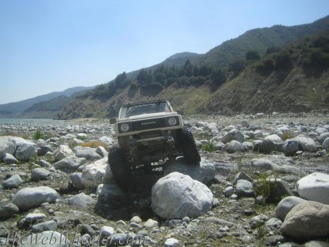 1987 Suzuki Samurai - A 1987 Suzuki Samurai navigates a rocky terrain next to a body of water under a clear blue sky.