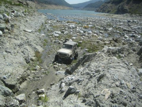 1987 Suzuki Samurai - Suzuki Samurai tackling rough terrain near a large body of water.