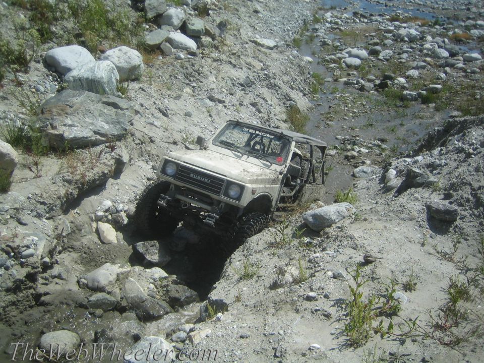Tan 1987 Suzuki Samurai navigating a rocky, wet terrain