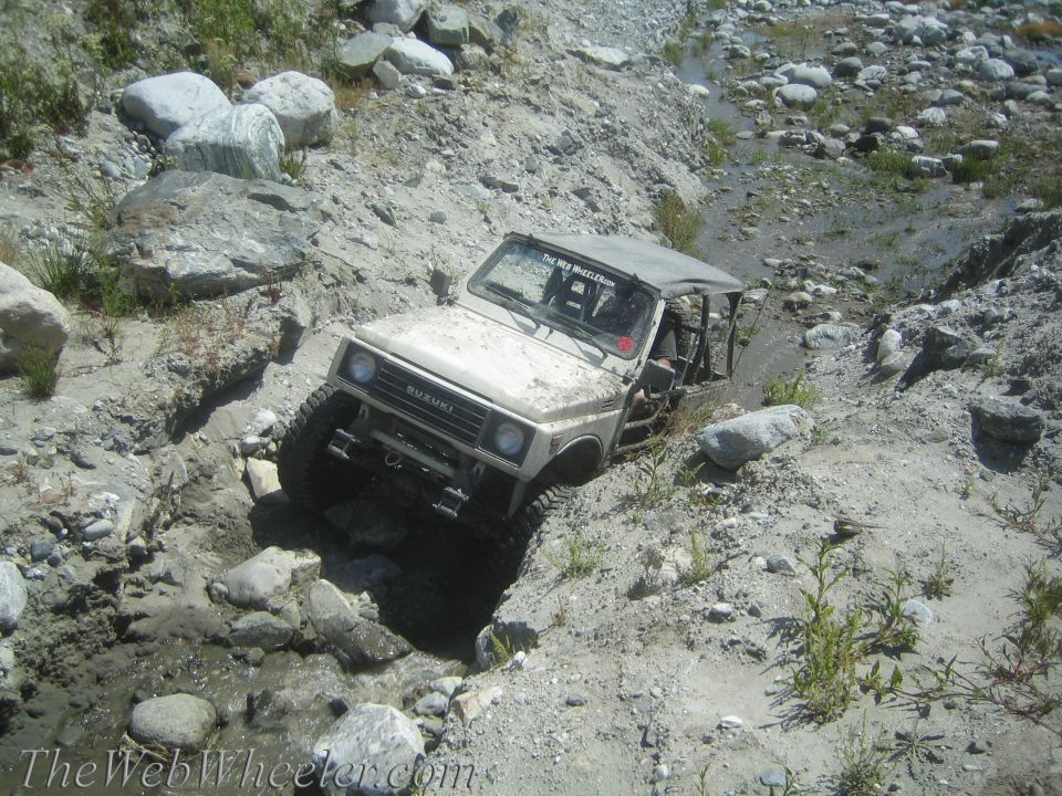 1987 Suzuki Samurai navigating a rocky, dry stream bed with a soft top