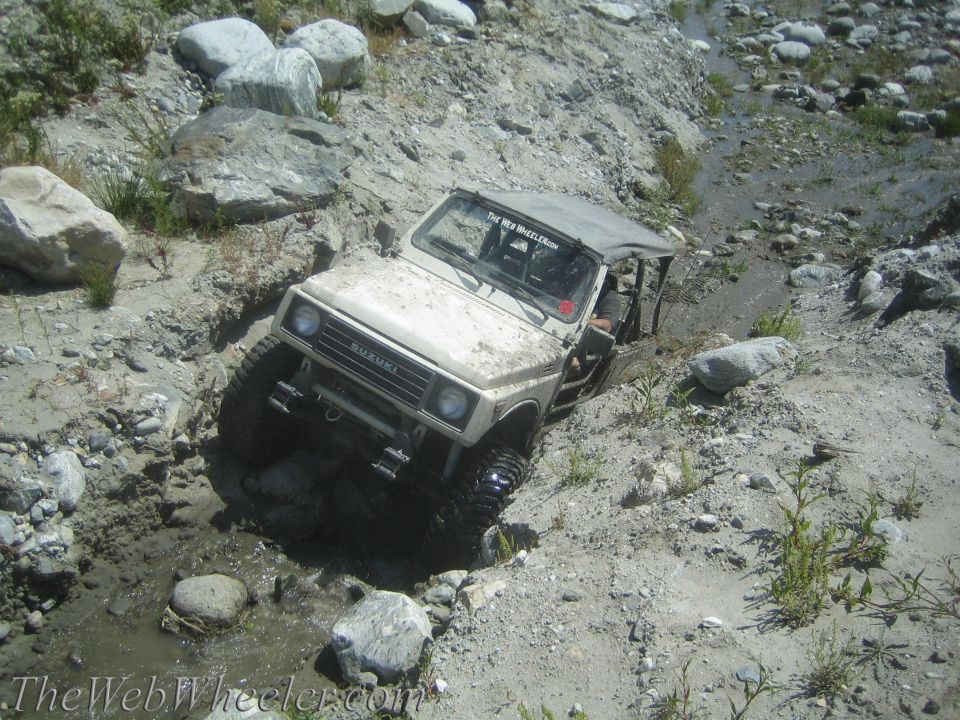 Suzuki Samurai navigating a muddy, rocky ditch. The Web Wheeler.com sticker on the windshield