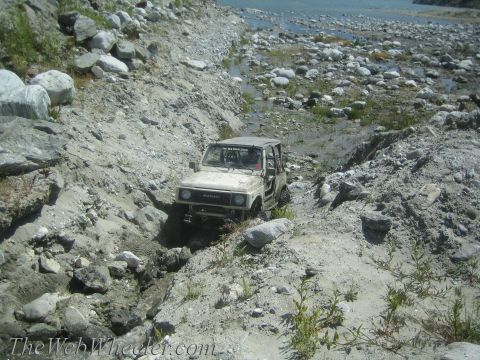 1987 Suzuki Samurai - A Suzuki Samurai navigates a challenging off-road path near a body of water.