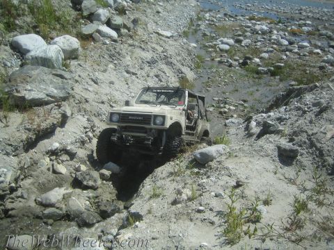1987 Suzuki Samurai - A tan 1987 Suzuki Samurai tackles a challenging off-road course through a rocky, dry riverbed.