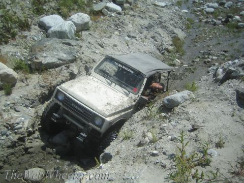 1987 Suzuki Samurai - A white 1987 Suzuki Samurai navigates a challenging off-road terrain with steep, rocky inclines.