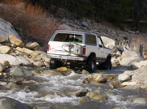 1986 Ford Bronco - Ford Bronco navigates a rocky stream bed, demonstrating off-road capability.