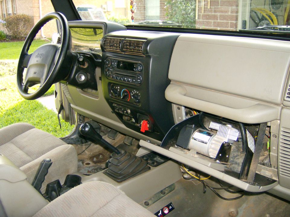 Jeep Wrangler interior showing dashboard, steering wheel, shifter, and an air compressor installed in the glove compartment