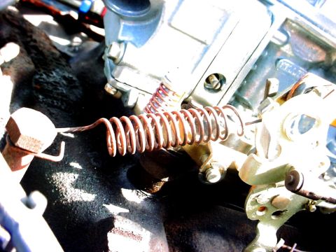 1992 Ford Mustang - A close-up view of engine carburetor linkage with a rusty spring.