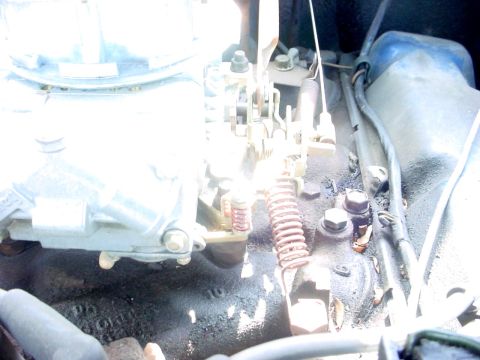 1992 Ford Mustang - A close-up view of the carburetor and associated engine parts, showing the throttle linkage and a spring mechanism.