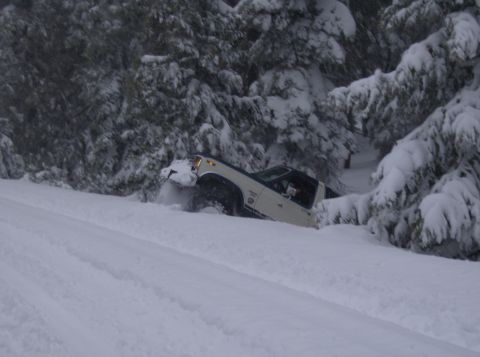 1986 Ford Bronco - A white SUV is stuck in deep snow on a wooded slope during a snowfall.