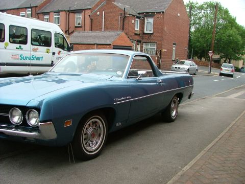 1970 Ford Ranchero - A blue 1970 Ford Ranchero is parked on a residential street next to a white van.