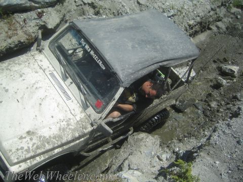 1987 Suzuki Samurai - A driver rests inside a white 1987 Suzuki Samurai after it became stuck in mud and rocks.