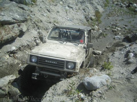 1987 Suzuki Samurai - This Suzuki Samurai is tackling a challenging off-road trail with steep, rocky inclines and muddy terrain.