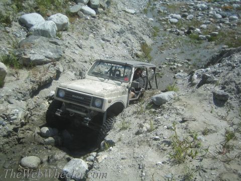 1987 Suzuki Samurai - Suzuki Samurai tackling a challenging off-road course with steep inclines and water obstacles.