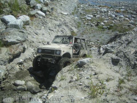 1987 Suzuki Samurai - A Suzuki Samurai tackles a challenging off-road course, with water and rocks creating obstacles.