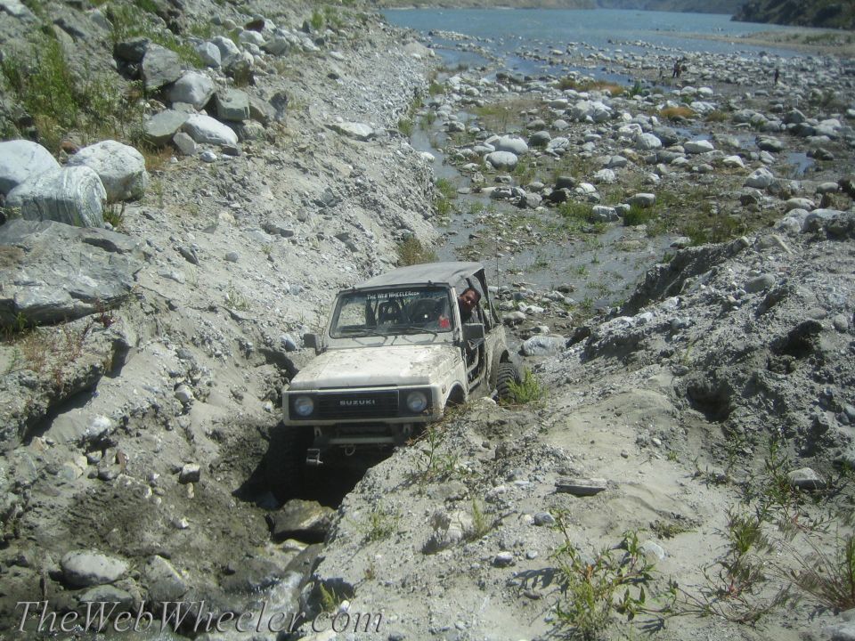 White Suzuki Samurai off-roading on a rocky, dry riverbed