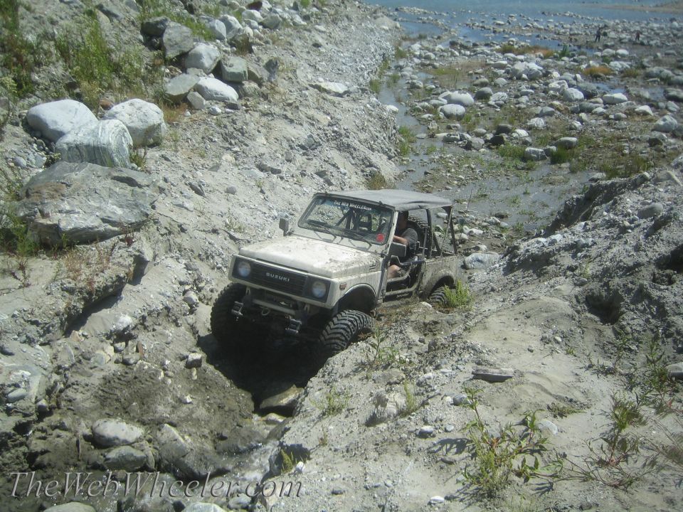 Tan 1987 Suzuki Samurai off-roading in a rocky dry riverbed