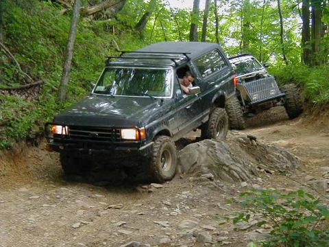1990 Ford Bronco - A 1990 Ford Bronco tackles a challenging off-road course, with a second vehicle following closely.