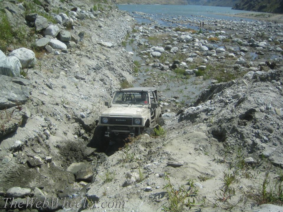1987 Suzuki Samurai navigating a muddy, rocky trail next to a river