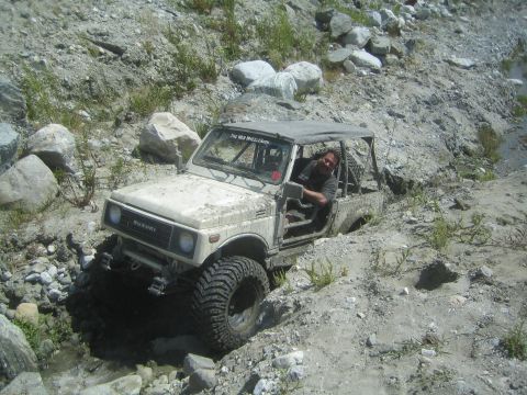 1987 Suzuki Samurai - A white Suzuki Samurai navigates a challenging off-road terrain with a driver inside.