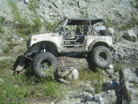 1987 Suzuki Samurai - This modified Suzuki Samurai is navigating a challenging off-road obstacle, balancing on a large log.