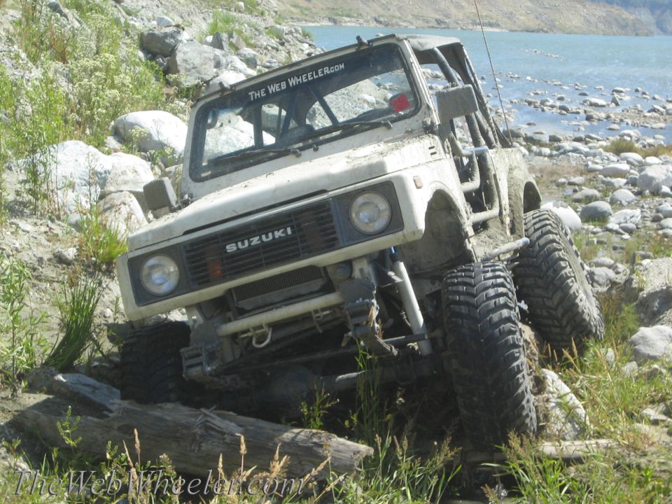 White 1987 Suzuki Samurai off-roading on a rocky shore