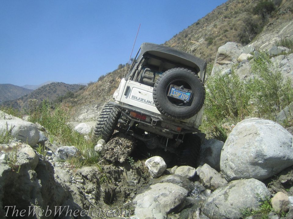 1987 Suzuki Samurai navigating a rocky, muddy stream bed on a mountain trail