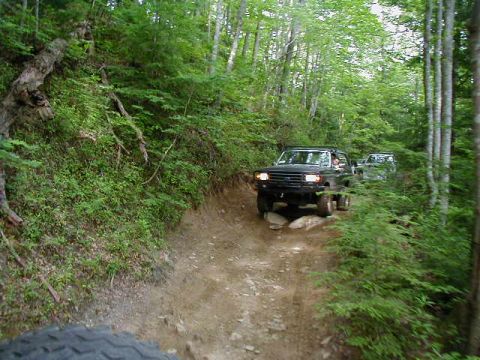 1990 Ford Bronco - Two off-road vehicles navigate a steep, wooded trail.