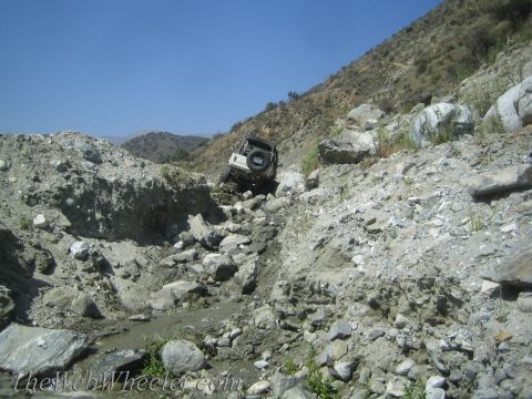 1987 Suzuki Samurai - A white 1987 Suzuki Samurai tackles a challenging off-road path through a rocky, dry creek bed.