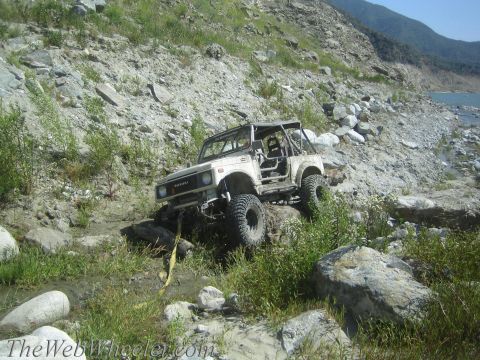 1987 Suzuki Samurai - Suzuki Samurai tackling challenging off-road terrain with a water body in the background.