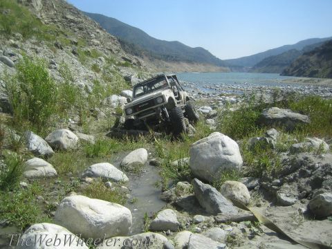 1987 Suzuki Samurai - A 1987 Suzuki Samurai is shown off-roading through a rocky, overgrown area next to a body of water.