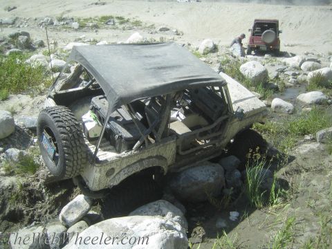 1987 Suzuki Samurai - Two Suzuki Samurai vehicles navigate a rocky, muddy terrain, with one appearing stuck in a stream.