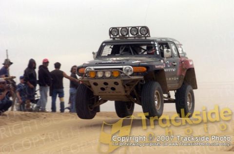 1992 Ford Explorer - Modified off-road SUV airborne over sand, with spectators observing the action.