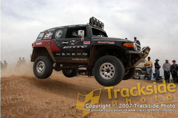 Toyota FJ Cruiser mid-air jump during off-road race, with spectators and another vehicle in background