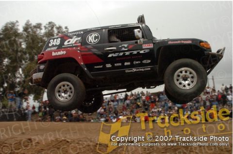 1992 Ford Explorer - A black Toyota FJ Cruiser is captured mid-air during a race event, with spectators in the background.