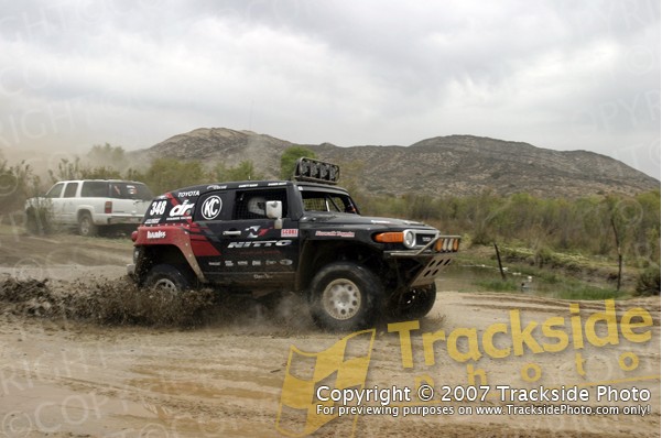 Black Toyota FJ Cruiser driving through mud, with a white SUV in the background