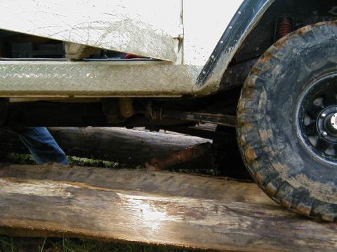 1990 Ford Bronco - A close-up side view shows the fender and large tire of a white SUV, which appears to be off-roading on logs.