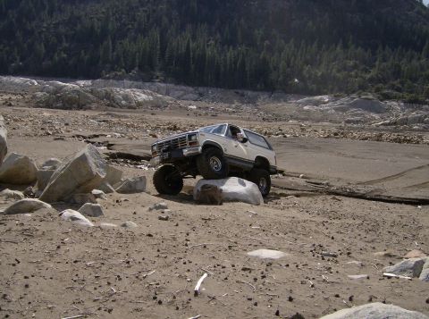 1986 Ford Bronco - Ford Bronco tackling rough terrain with a driver visible inside.