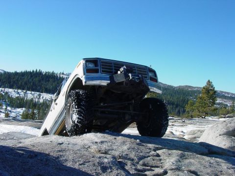 1986 Ford Bronco - This modified SUV is navigating a rocky, snow-dusted terrain under a clear blue sky.