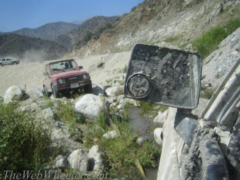 1987 Suzuki Samurai - Two off-road vehicles navigate a challenging, rocky terrain in a mountainous area.