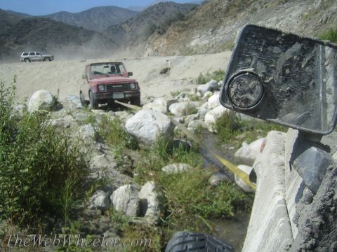 1987 Suzuki Samurai - A red 1987 Suzuki Samurai is being towed out of a rocky riverbed, with another SUV in the background.