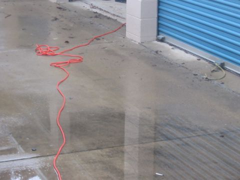 1991 Ford Bronco - An orange extension cord snakes across a wet concrete surface next to a storage unit door.